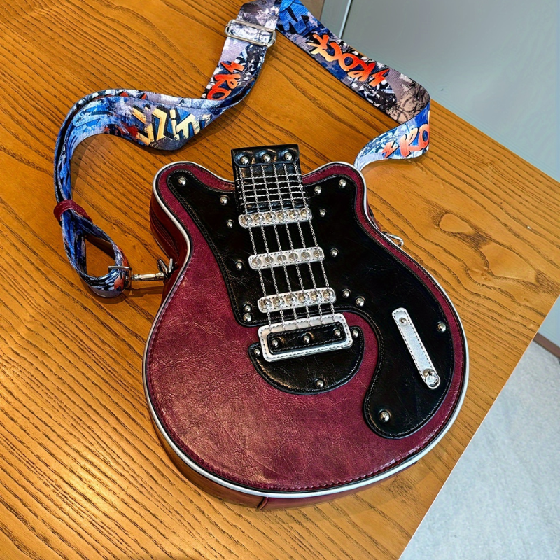 Bordowa torebka Guitarista Crossbody z Inicala.pl lezy na drewnianym stole z czarnym frontem polyskujacymi lancuszkami i szerokim kolorowym paskiem w stylu ROCK
