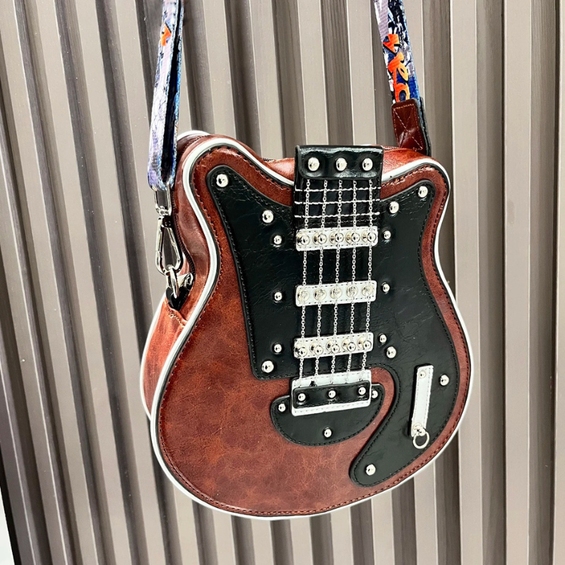Guitarista torebka crossbody w kolorze koniakowego brazu zawieszona na pasku ROCK przed sciana paneli czarny front w ksztalcie gitary metalowe lancuszki i srebrne nity rockowy dodatek z Inicala.pl