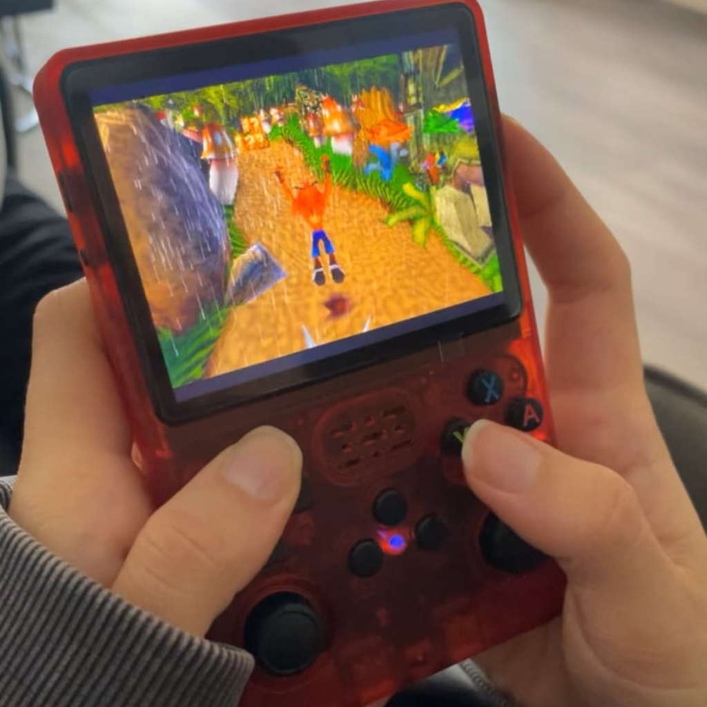PixelPlay™ Legends od Inicala.pl – przenośna konsola retro w czerwonej, półprzezroczystej obudowie. Na ekranie gra Crash Bandicoot. Kompaktowa, mocna i gotowa do grania w klasyki gdziekolwiek jesteś.