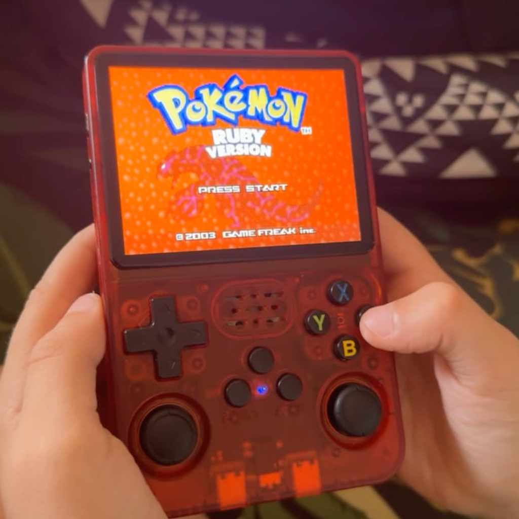 PixelPlay™ Legends od Inicala.pl w czerwonej wersji, trzymana w dłoniach podczas gry Pokémon Ruby. Kompaktowa konsola retro z tysiącami klasyków w jednym urządzeniu.